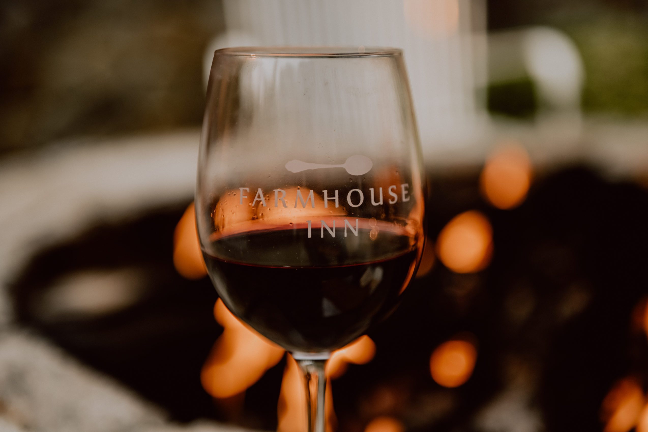 Farmhouse Inn branded wine glass with red wine in front of fire