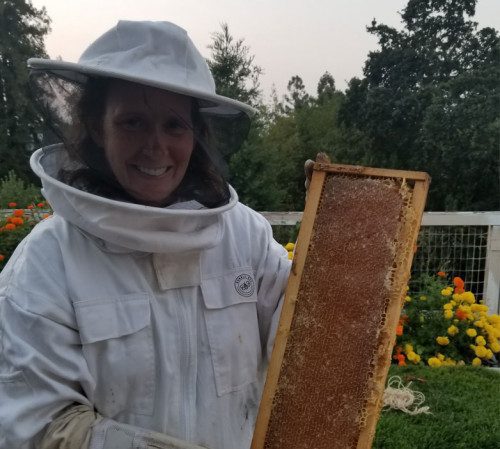 image of women in beekeeping outfit holding an honeycomb