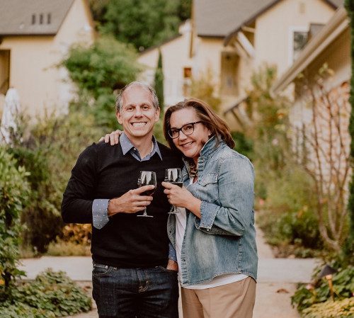 joe and Catherine holding smiling together in front of the property and holding glasses of wine