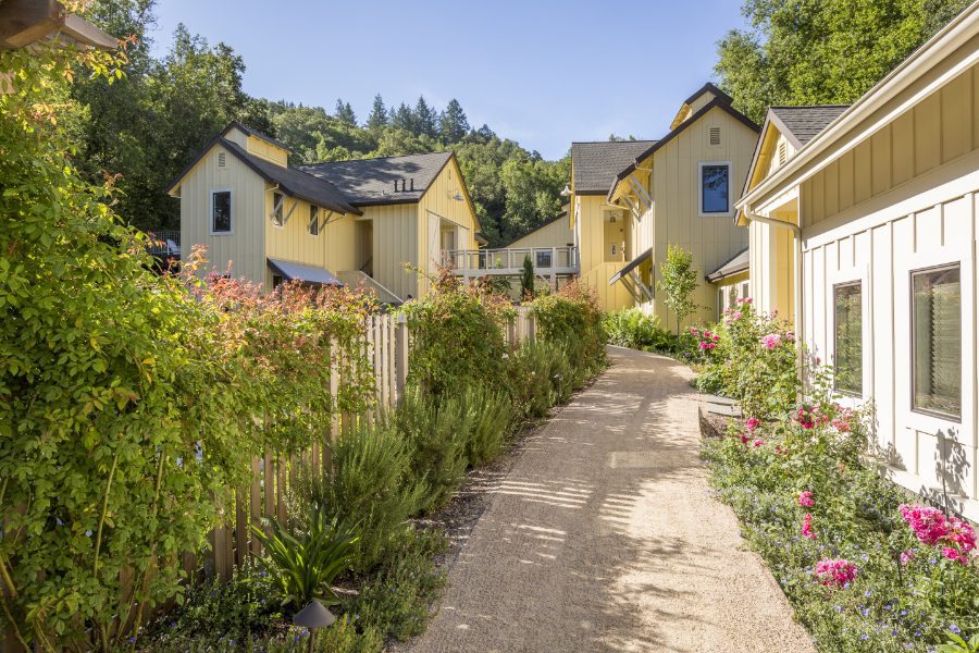 Quaint pathway on the perimeter of one of the Farmhouse Inn buildings surrounded by lush greenery and pink flowers.