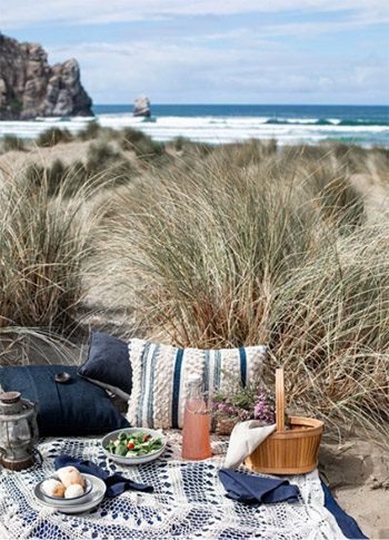 picnic blanket setup near the ocean with food settings and basket