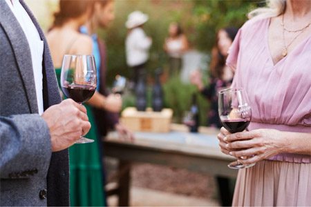 casual photo of a man and woman conversing at wine tasting, holding glasses of red wine.