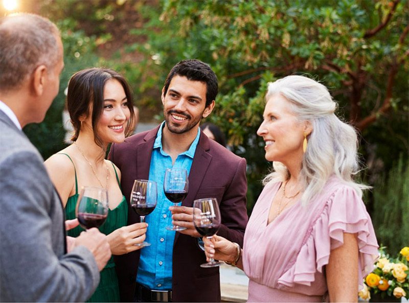 Two men and two women in formal attire outside conversing at wine tasting.