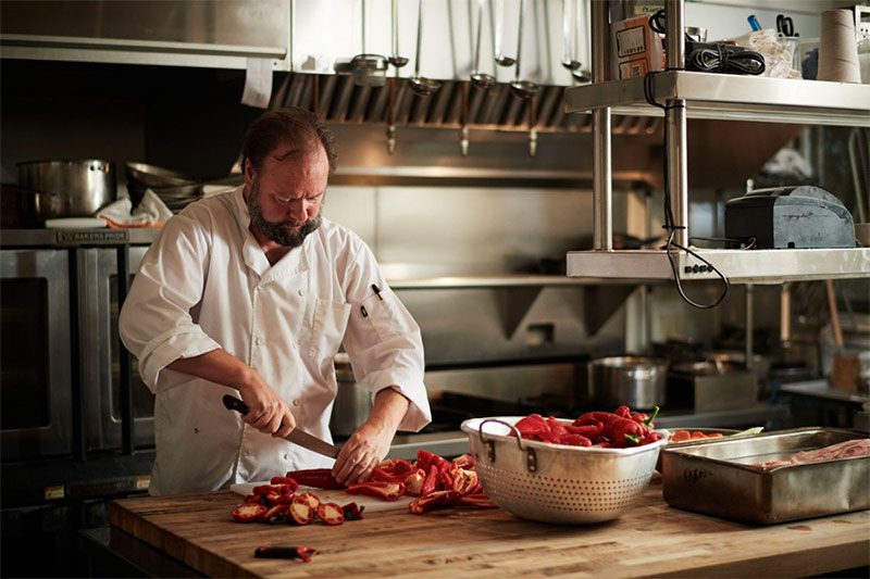 Chef in kitchen of Farmhouse restaurant chopping vegetables and placing in a large metal bowl.
