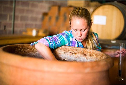 Woman reaching into a large ceramic pot holding a long skinny glass with liquid in it.