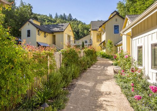 Quaint pathway on the perimeter of one of the Farmhouse Inn buildings surrounded by lush greenery and pink flowers.