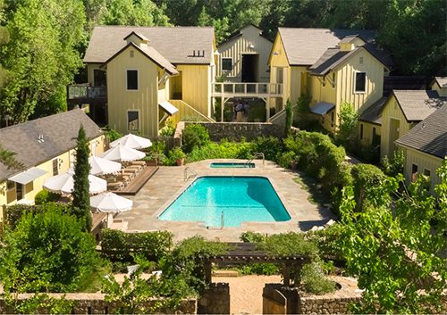 Aerial view of center of Farmhouse Inn. Yellow buildings with swimming pool in the middle and some greenery surrounding the area.