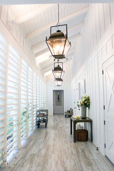 Hallway of the Farmhouse Spa. Windows with blinds on the left, wood floors, elegant lantern lights above and white wood walls.