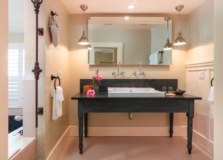 Interior of Farmhouse Room bathroom: Large double sink with black table and large mirror hung above.