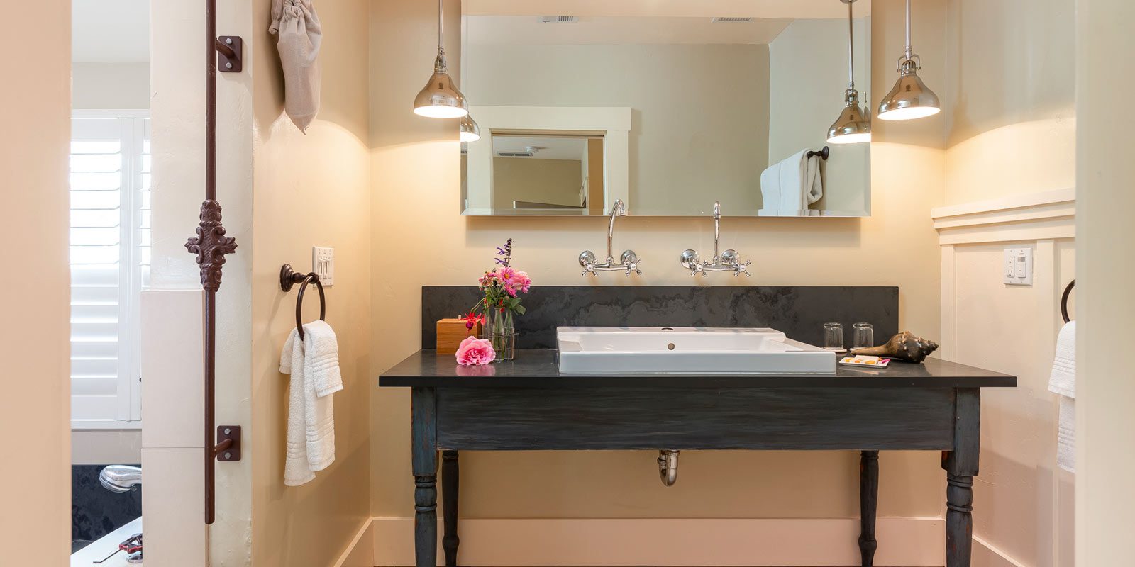 Interior of Farmhouse Room bathroom: Large double sink with black table and large mirror hung above.