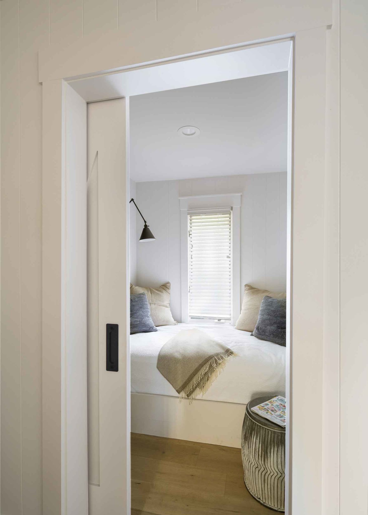 vertical view looking into the doorway of the Cottage Petite Suite. partial view of wood floor large bed with white bedding with four matching pillows and narrow window with light blinds