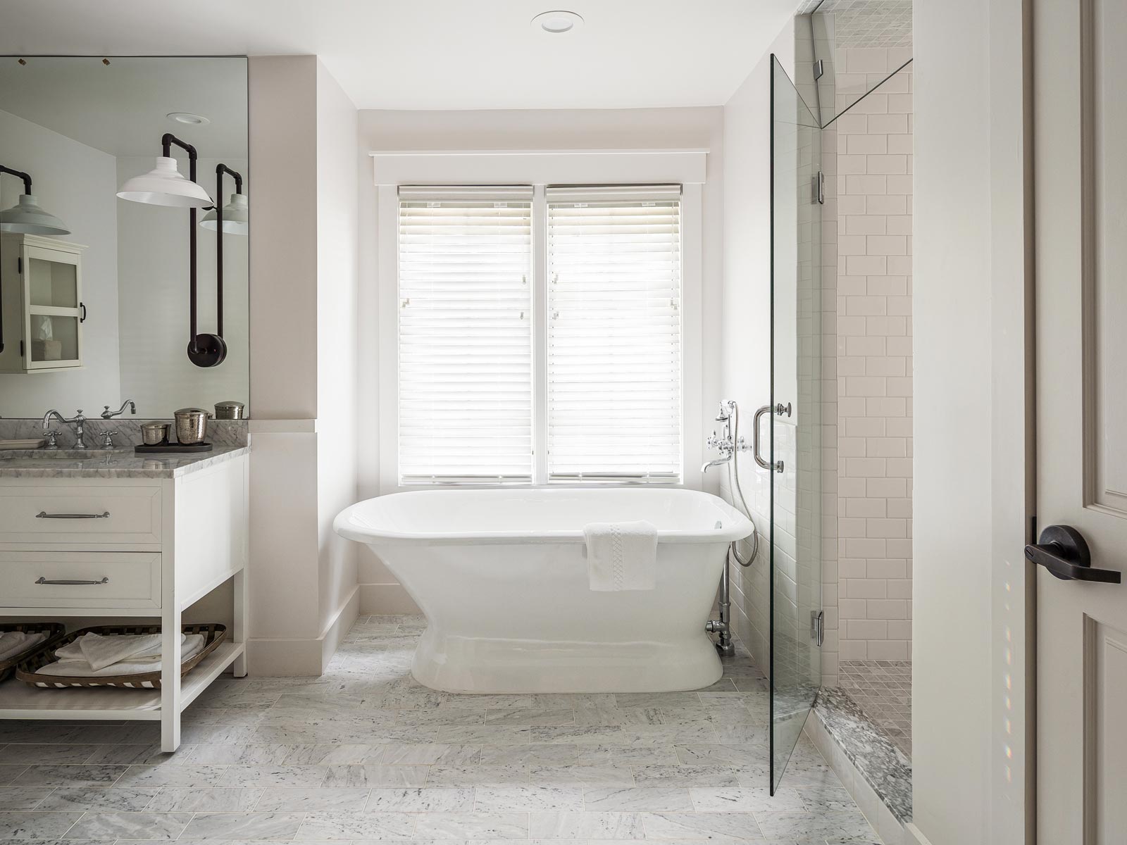 Bathroom photo inside the Cottage Petite Suite. white standalone bathtub, shower with glass door, light colored floor tiles, white modern vanity with two drawers and large mirror to ceiling.