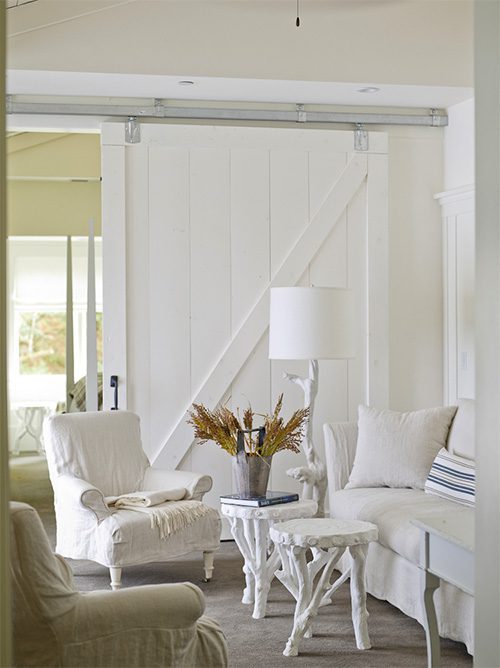 Interior of Barn One Bedroom Suite: White wood partition sliding door in back, white cushioned chair and loveseat with white corner lamp and two small coffee tables.