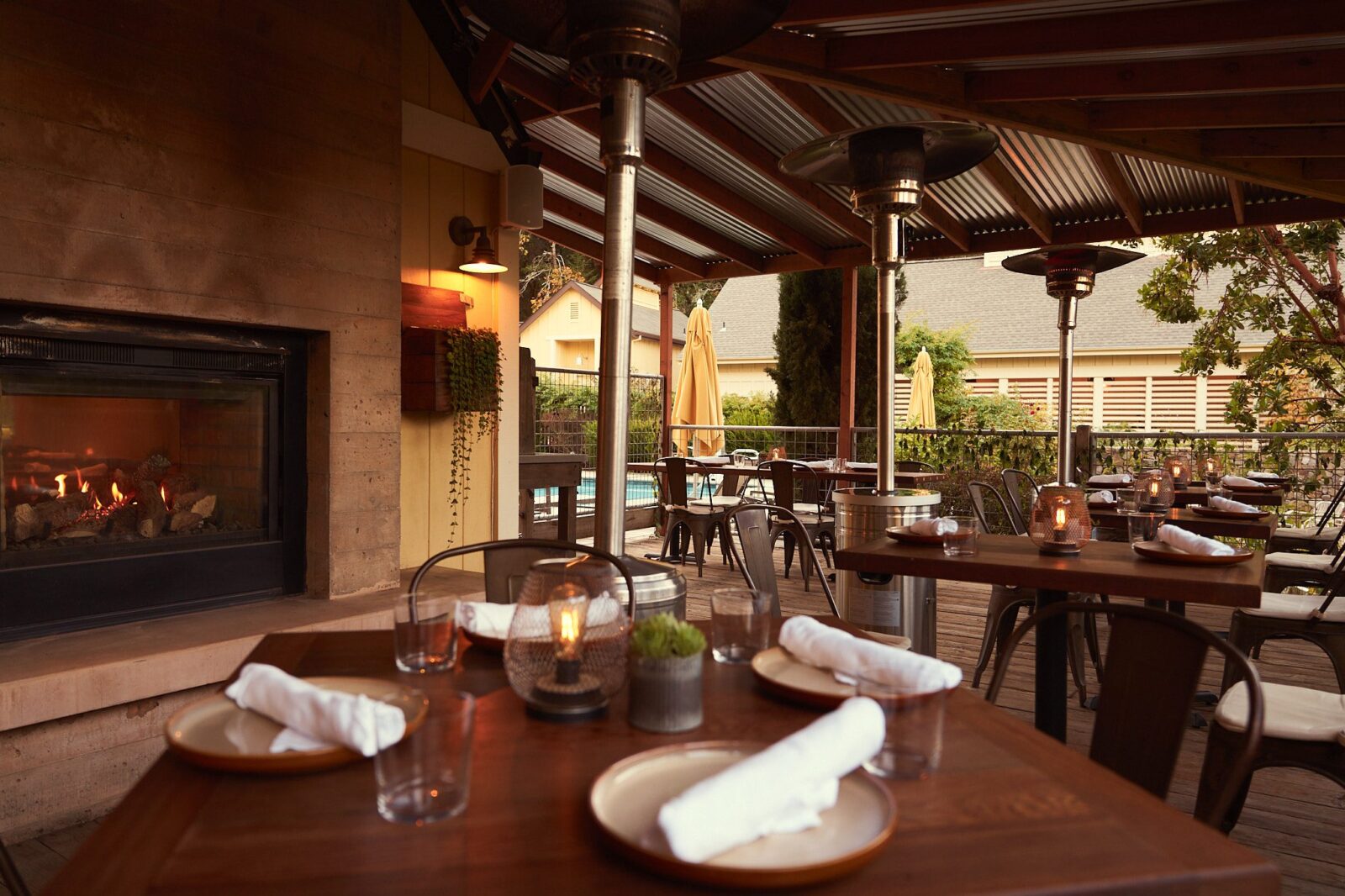 close-up of an outdoor four seated table outside The Farmstand. Four wicker seats, brown placemats, whote plates, two wine glasses along with salad and pizza.