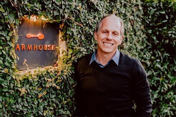 Joe Bartolomei smiling next Farmhouse Inn sign