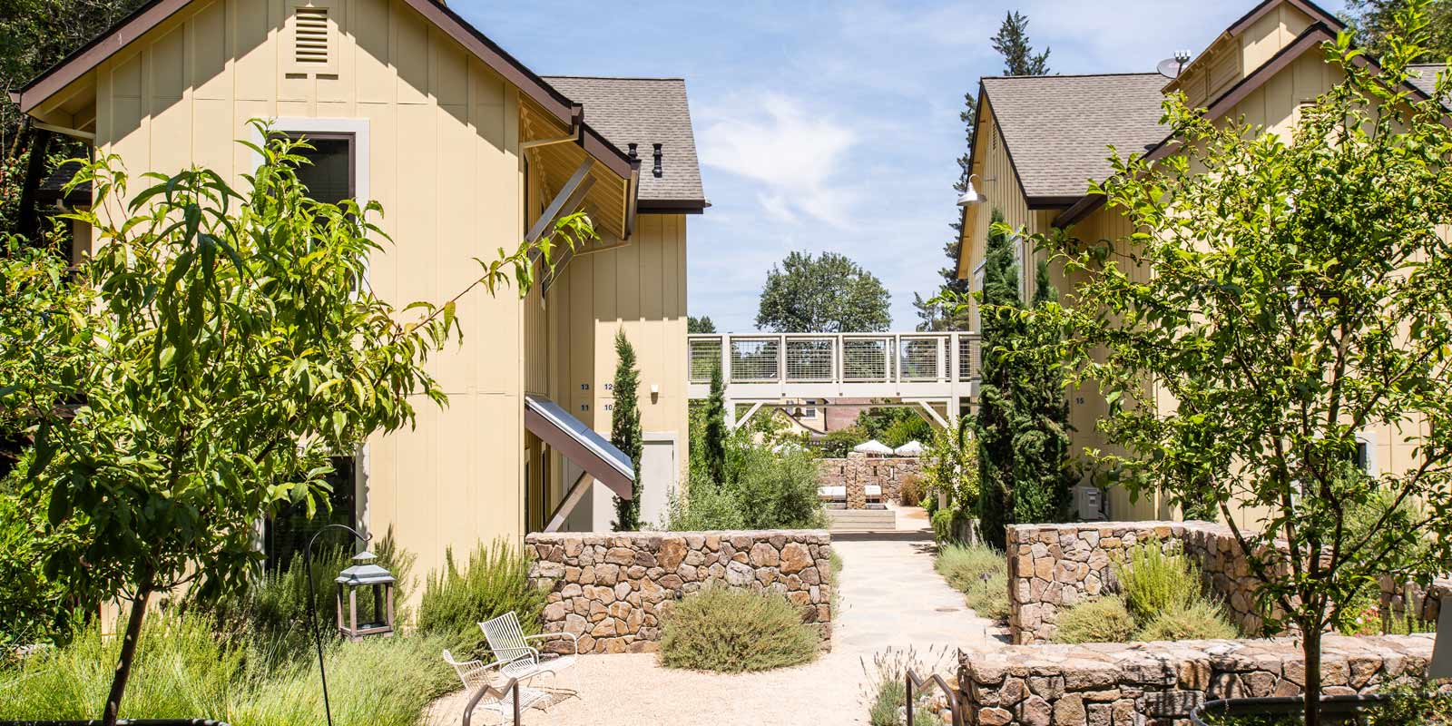 Exterior view of Farmhouse Inn: two-story yellow buildings on left and right with catwalk running in between and concrete path underneath.