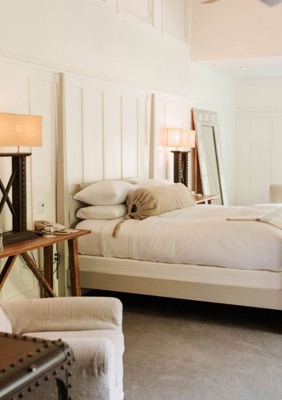 Interior view of the barn junior suite: Large bed with white bedding and four pillows, tall white headboard and nightstand with lamp.