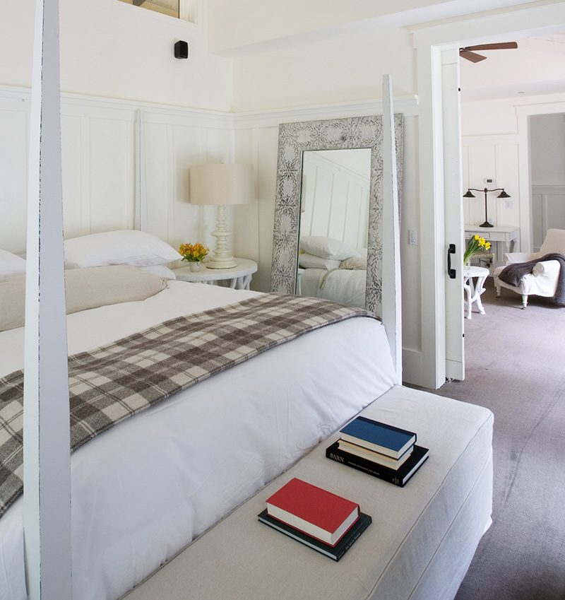 inside the Barn One Bedroom Suite showing king-sized bed with white bedding and large stand-up mirror and lamp.