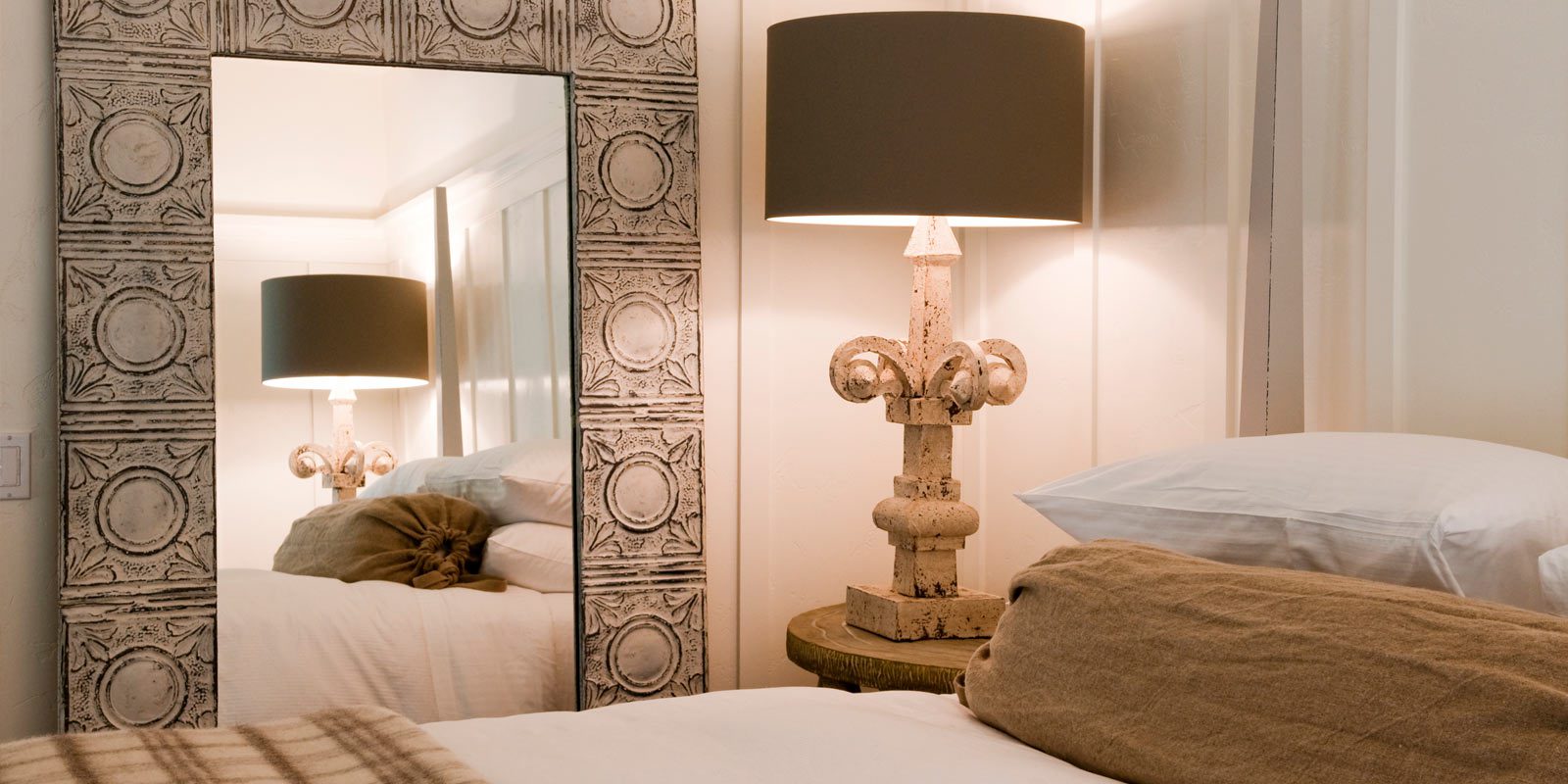 Interior close-up of Barn Junior Suite. Large bed with white bedding, tall, ornate lamb on night stand, large wall mirror with decorated frame.