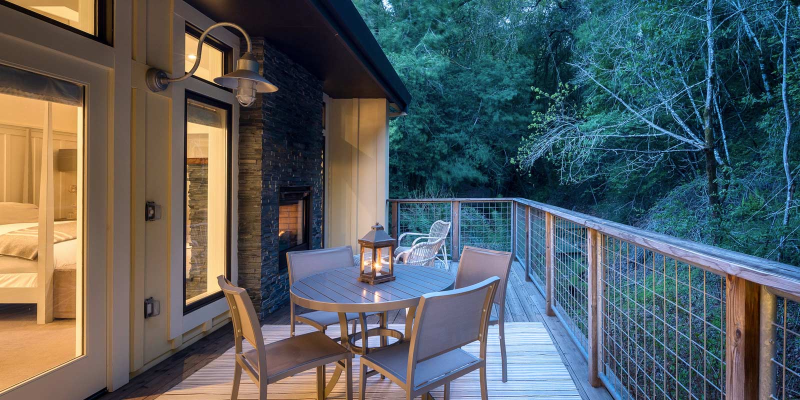 Elevated wood porch of Barn One Bedroom Suite with round patio table with chairs, wood bannister with greenery in back and glimpse into the room.