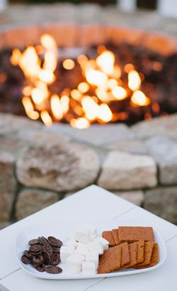close-up of s'mores on a white plate with a stone fire-pit with fire lit in the background.