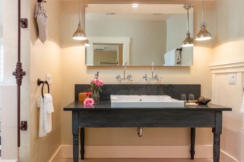 Interior of Farmhouse Room bathroom: Large double sink with black table and large mirror hung above.