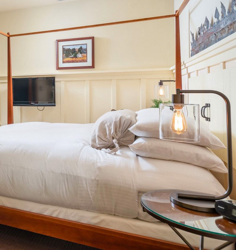 Interior of Farmhouse room: large bed with brown wood bedframe and bed posts, ornate wood moulding on walls and farmed picture on wall.