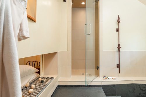 Interior of Farmhouse bathroom: full glass shower door with beige walls and tile floors.