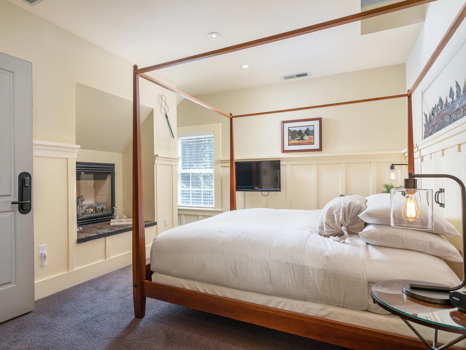 Interior of Farmhouse room: large bed with brown wood bedframe and bed posts, ornate wood moulding on walls and farmed picture on wall.