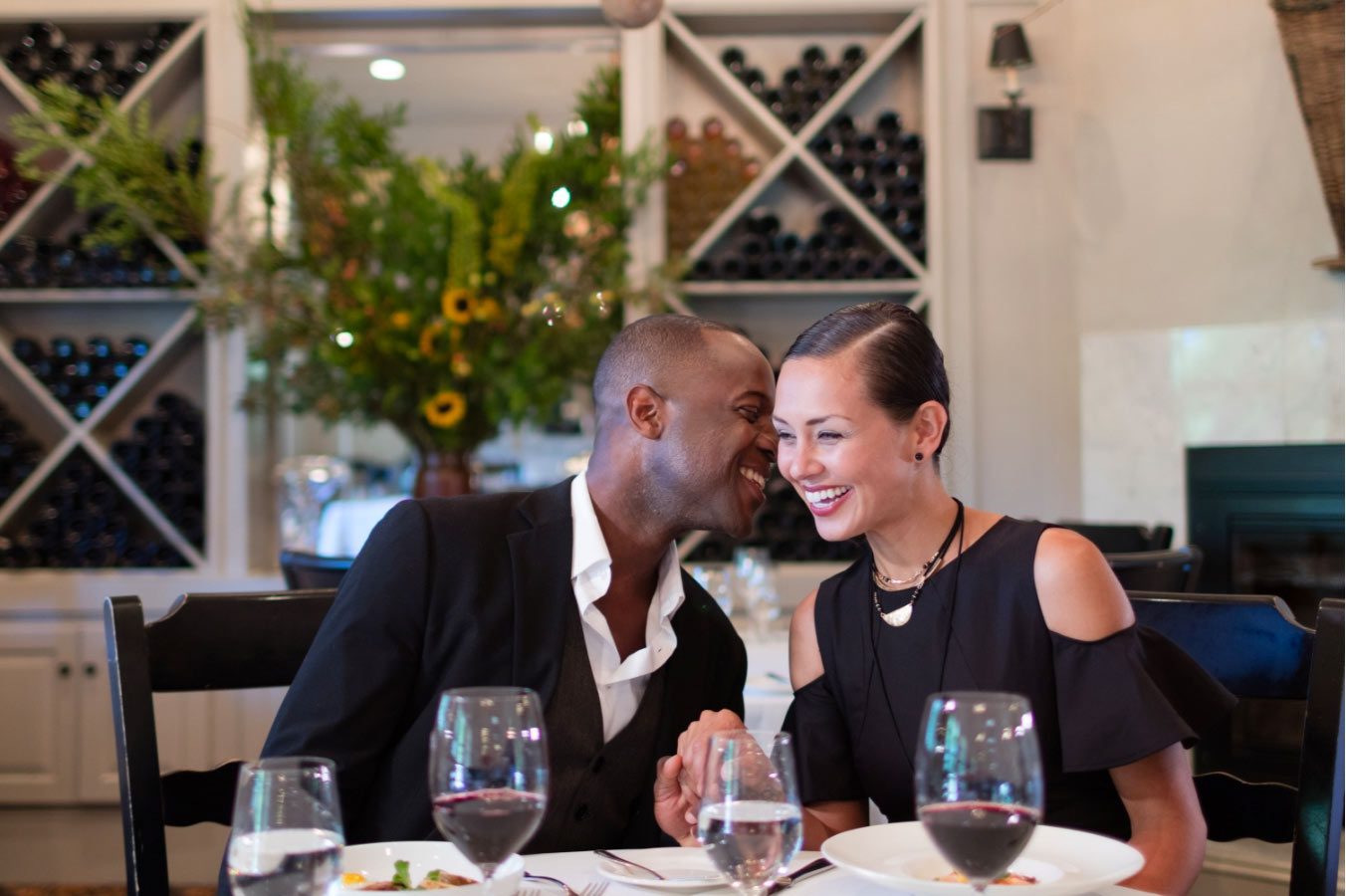 man and woman drinking wine at restaurant and man is whispering in womans ear and laughing