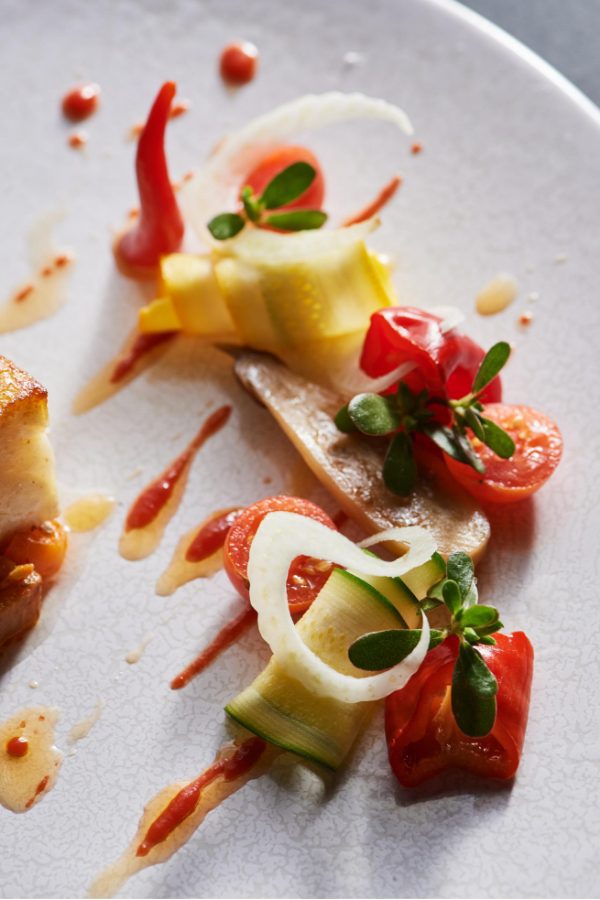 piece of roasted fish on white plate with vegetable garnish, sauces