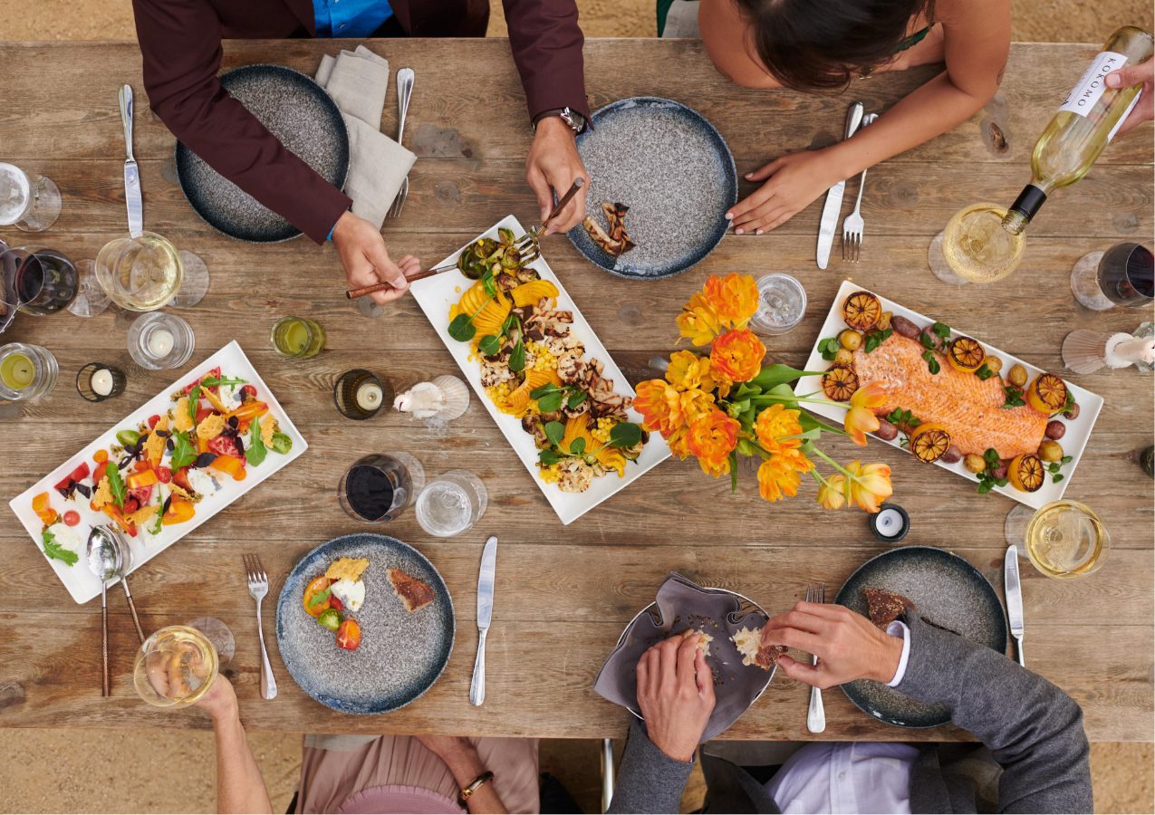 overhead view of wood table with 3 plates of appetizers and several people's place settings