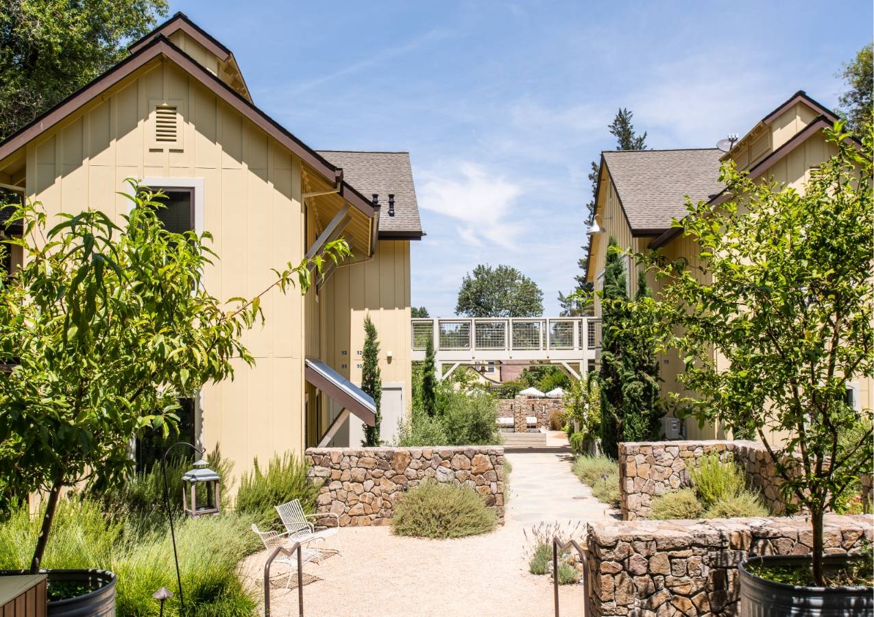 Exterior view of Farmhouse Inn: two-story yellow buildings on left and right with catwalk running in between and concrete path underneath.