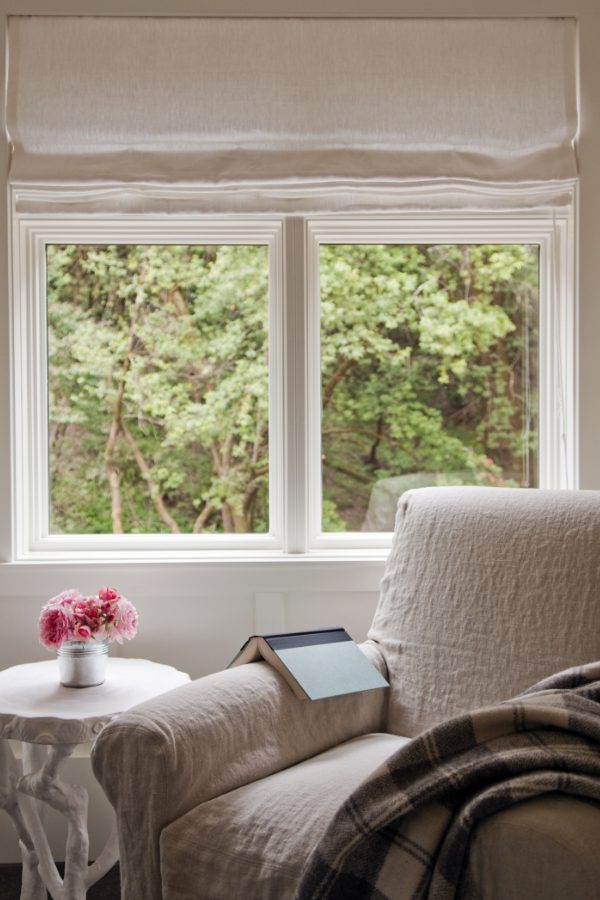 Farmhouse room with plush white chair, plaid blanket, and book against a bright lit window
