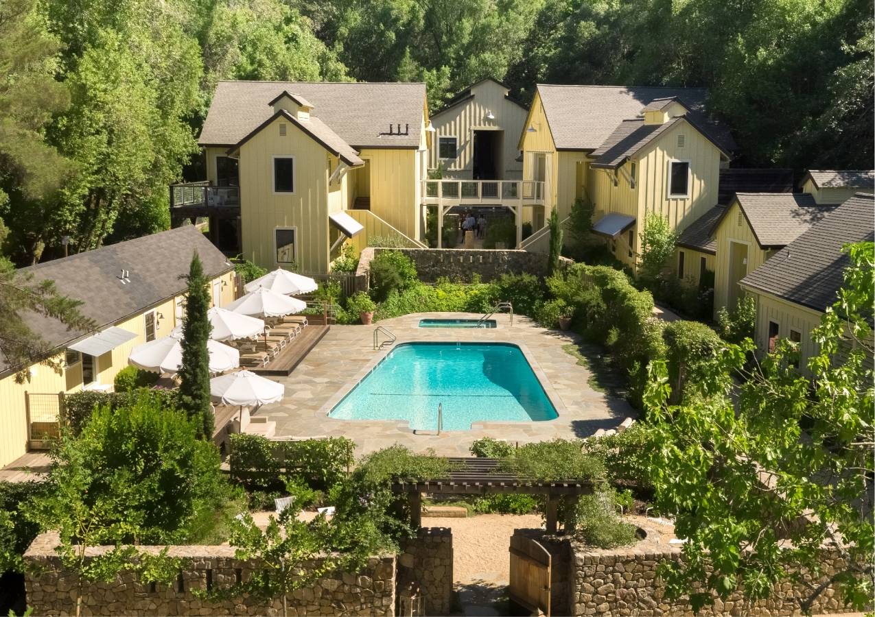 Aerial view of center of Farmhouse Inn. Yellow buildings with swimming pool in the middle and some greenery surrounding the area.