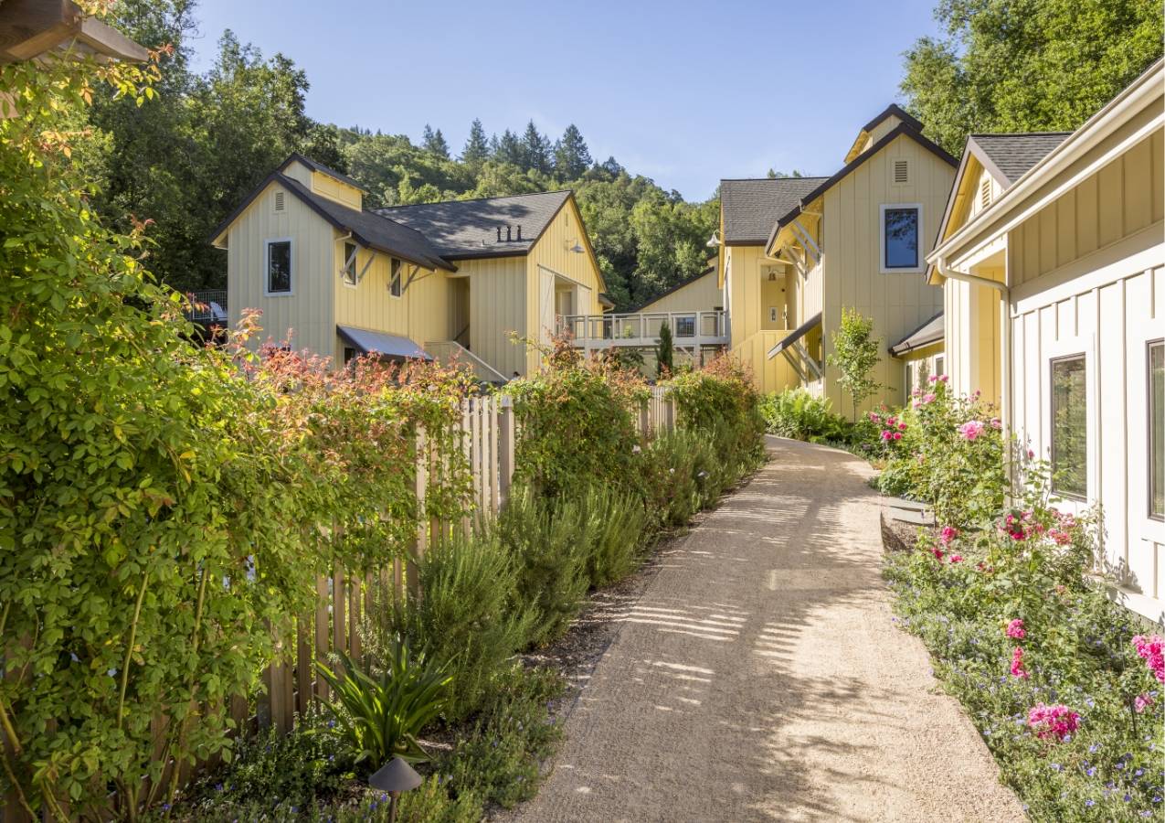 Quaint pathway on the perimeter of one of the Farmhouse Inn buildings surrounded by lush greenery and pink flowers.