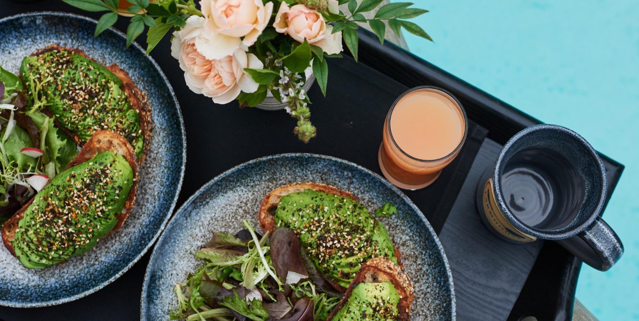 An overhead view of a dark tray with two elegantly plated salads, with flowers next to pool.