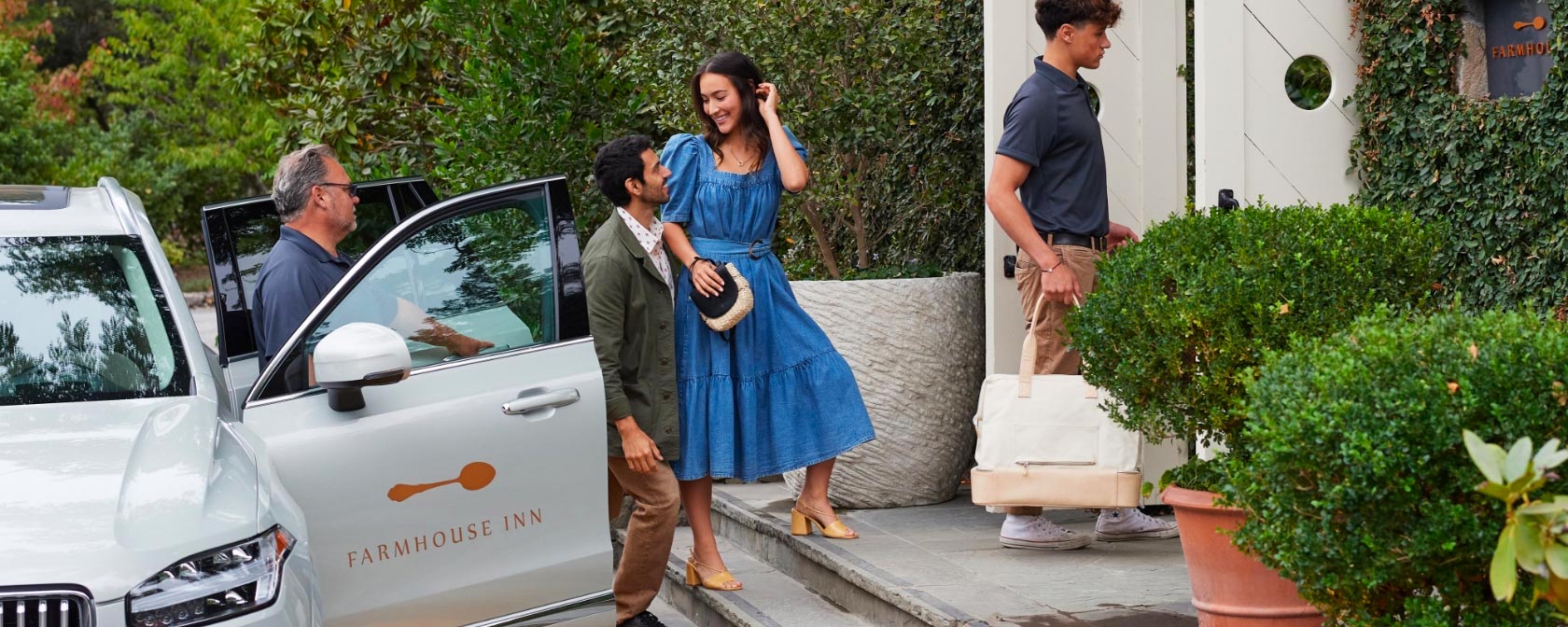 Man and woman in formal attire arriving at the Farmhouse Inn as they exit a car that has Farmhouse logo on it.