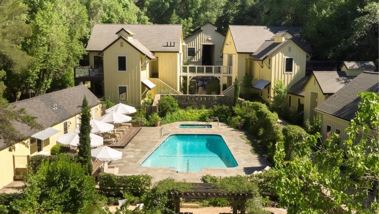 Aerial view of center of Farmhouse Inn. Yellow buildings with swimming pool in the middle and some greenery surrounding the area.