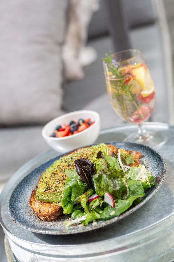 serving tray with avocado toast and side salad, bowl of mixed berries, and sparkling wine with a seasonal garnish