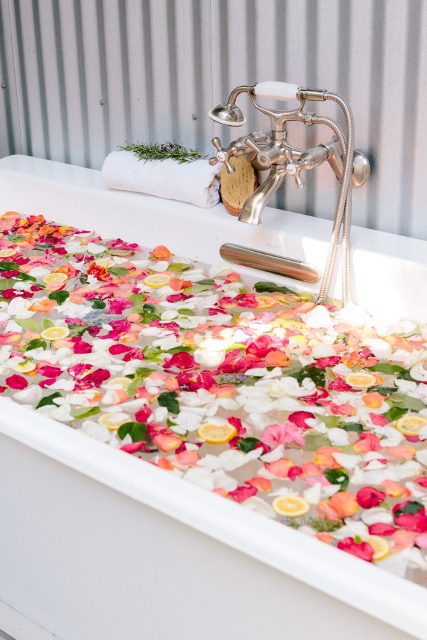 Close-up of bathtub faucet and bathtub with colorful flower pedals floating on the water