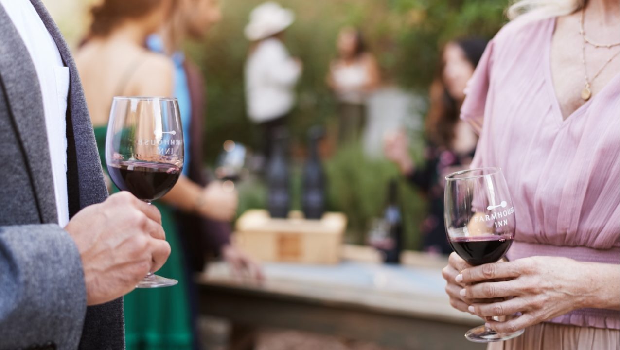 casual photo of a man and woman conversing at wine tasting, holding glasses of red wine.