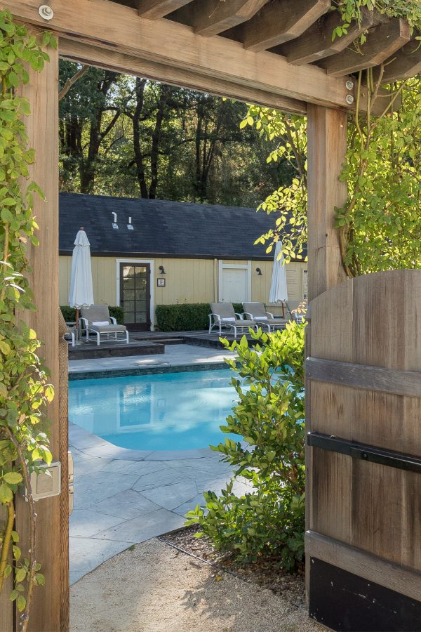 Farmhouse pool entrance: beautiful wood gate with green wines and shrubbery wrapping around. The grange in the background