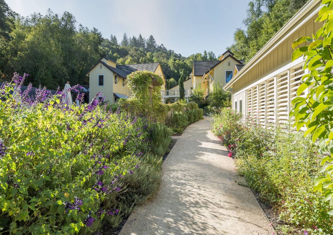 Quaint pathway on the perimeter of one of the Farmhouse Inn buildings surrounded by lush greenery and pink flowers.