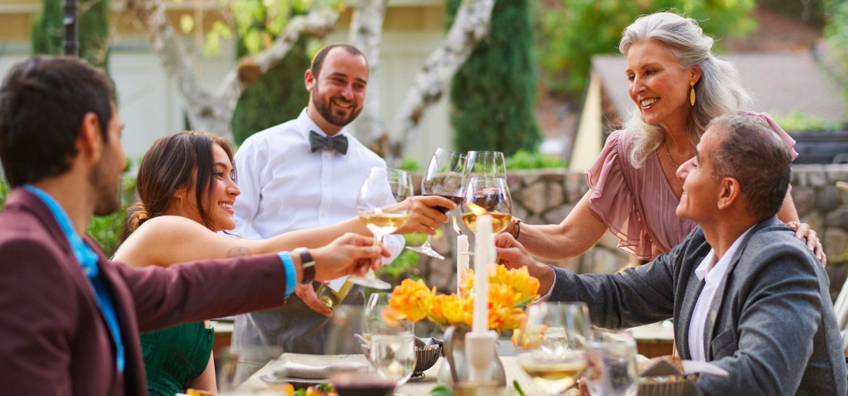 group of people toasting with wine around an outdoor dining table