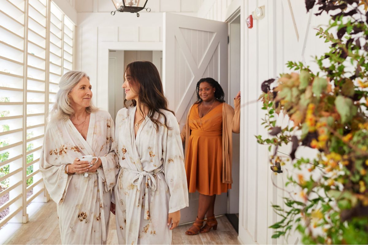 An older woman and younger woman walking happily in matching robes from the Farmhouse Inn Spa. The Spa keeper is in the background.