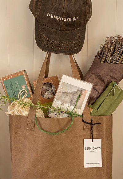 close-up of brown tote bag hanging on a hook with a Farmhouse Inn brimmed cap hanging above it.