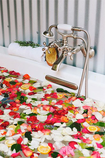 Close-up of bathtub faucet and bathtub with colorful flower pedals floating on the water