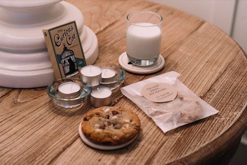 Hotel room table with candles, cookies, milk and a little book titled, 