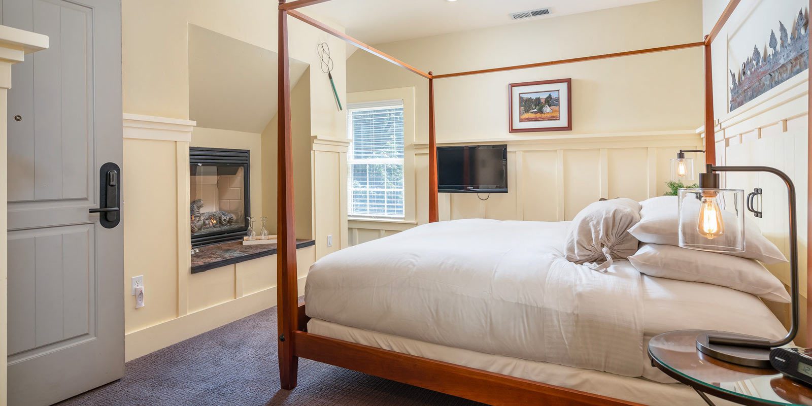 Interior of Farmhouse room: large bed with brown wood bedframe and bed posts, ornate wood moulding on walls and farmed picture on wall.